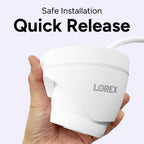 Hand holding a white Lorex quick-release security camera against a pale lavender background
